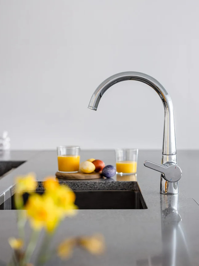 Robinet de cuisine chromé brillant, installé sur évier gris dans une cuisine épurée avec lumière naturelle