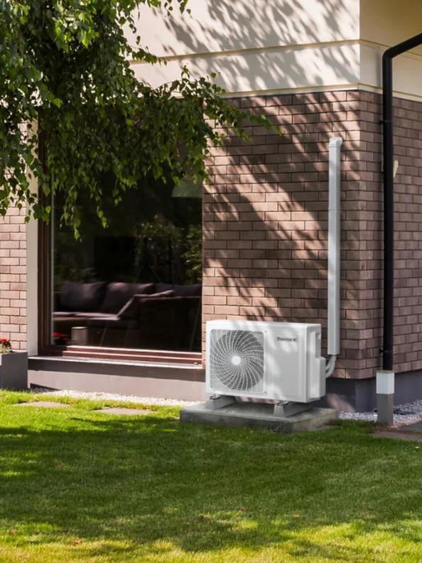 Unité extérieure de PAC installée contre une maison individuelle avec jardin, pour chauffage économique et performant.